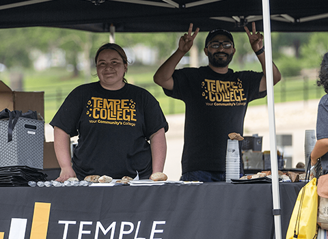 two individuals standing outdoors by a table booth with a sign that reads temple college workforce and continuing education